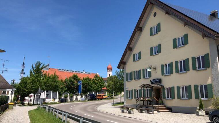 Gasthof-Front-mit-Maibaum-und-Kirche-im-Hintergrund Gasthof-Front-mit-Maibaum-und-Kirche-im-Hintergrund